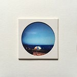 "Estoril", pièce unique 10 x 10 cm, signée au dos, faite à la main par la photographe. Image choisie, découpée, recadrée, insérée derrière le hublot protecteur, comme une loupe sur la miniature, fixée au papier canson, avec un espace de méditation neutre autour du cercle de l’image, le tout sur un support carton plume d’un centimètre d’épaisseur. Le motif circulaire est aussi un hommage à l’écrivain poète portugais Fernando Pessoa qui portait des lunettes cerclées. 