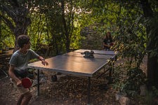 Deux enfants jouent au ping pong dans un jardin avec un chat installé sur la table de ping pong, Olargues, le 7 août 2024 