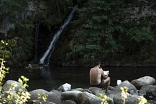 Un homme lit à l'ombre sur un rocher dans la fraicheur de la source du Frejo, Olargues, le 10 août 2024. 